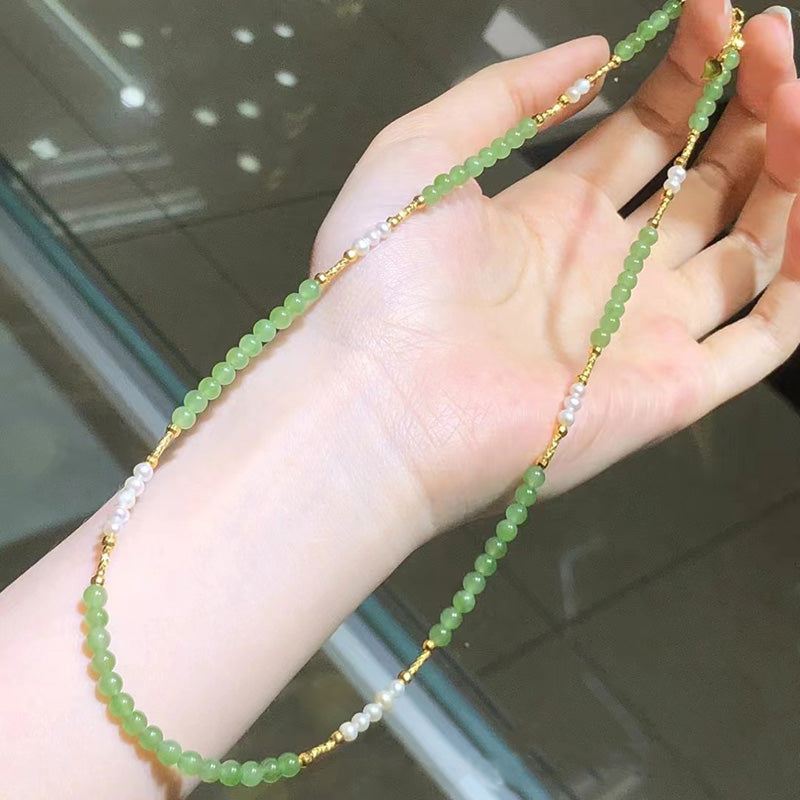 A delicate necklace featuring 18K gold, natural jadeite beads, and white pearl beads, held in a hand.
