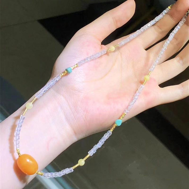 A delicate necklace featuring light - hued amethyst beads, complemented by a charming orange amber pendant, small turquoise and yellow bead accents, and gold - toned metal elements. Ideal for adding a touch of elegance to any ensemble