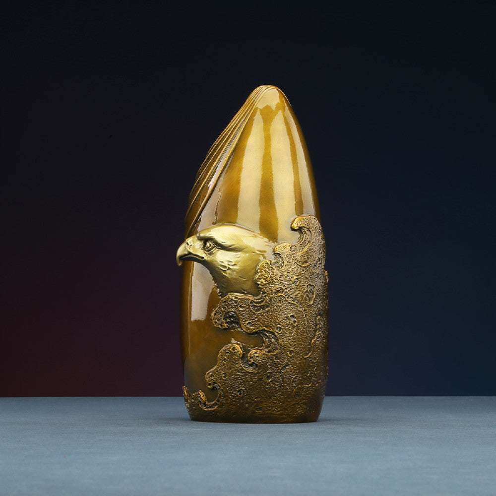 Brass eagle sculpture with textured details, placed on blue surface against dark gradient background