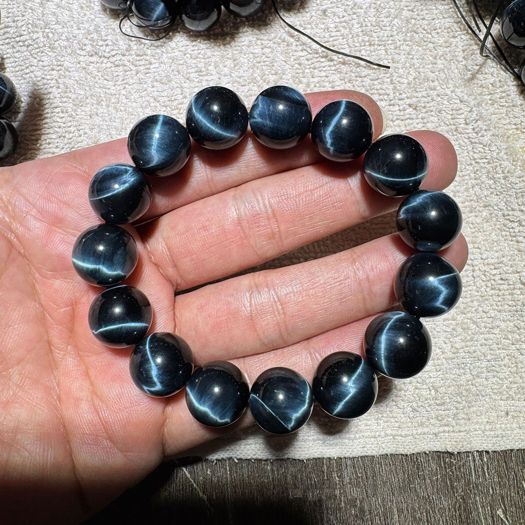 A black cat's eye gemstone bead bracelet held in a hand, showcasing round beads with distinct cat's eye effect stripes, creating a striking visual appearance.