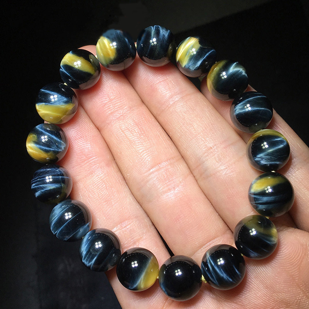 A black cat's eye gemstone bead bracelet held in a hand, showcasing round beads with distinct cat's eye effect stripes, creating a striking visual appearance 01