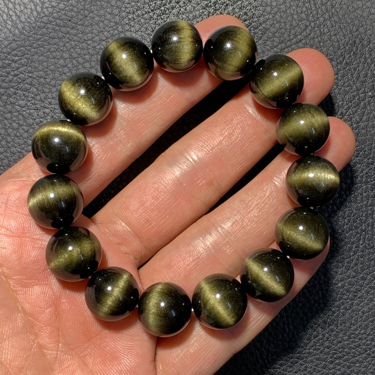 A black cat's eye gemstone bead bracelet held in a hand, showcasing round beads with distinct cat's eye effect stripes, creating a striking visual appearance.