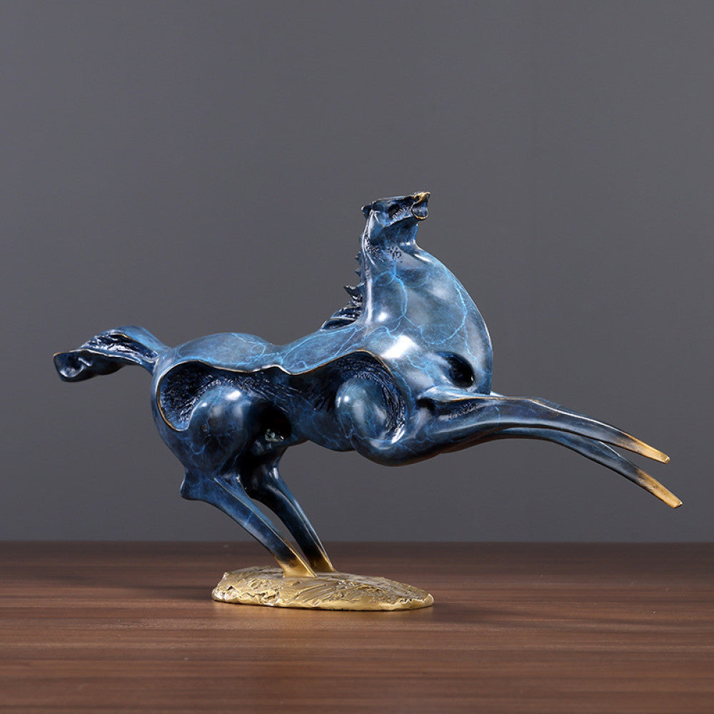 Blue galloping horses statue with golden accents, a symbol of success and strength in Feng Shui, displayed as stylish home decor on a wooden table against a gray background