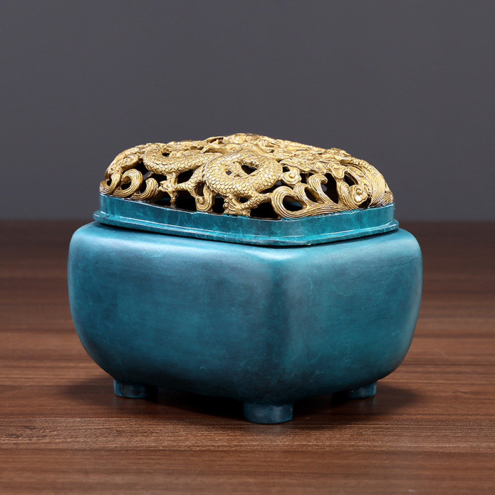 Blue-green bronze Chinese incense burner with intricately carved golden dragon pierced lid, square body, and small feet, a Feng Shui symbol of wealth and protection, displayed as a stylish home decor piece on a wooden surface against a gray background 01
