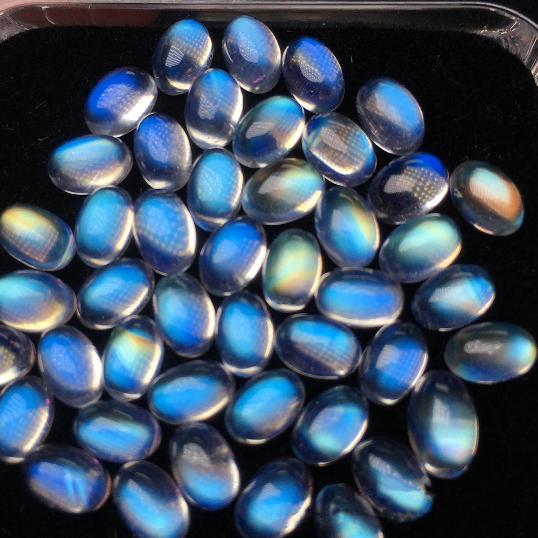 Oval moonstone on a black tray, with charming blue and white luster, suitable for jewelry design