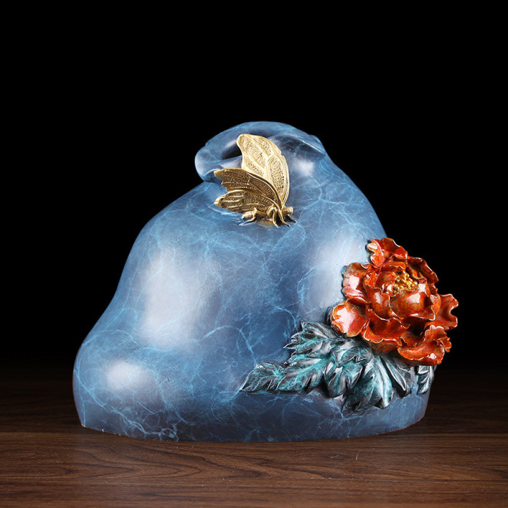 Blue textured decorative sculpture with brass butterfly and red peony flower details, displayed on wooden table against dark background