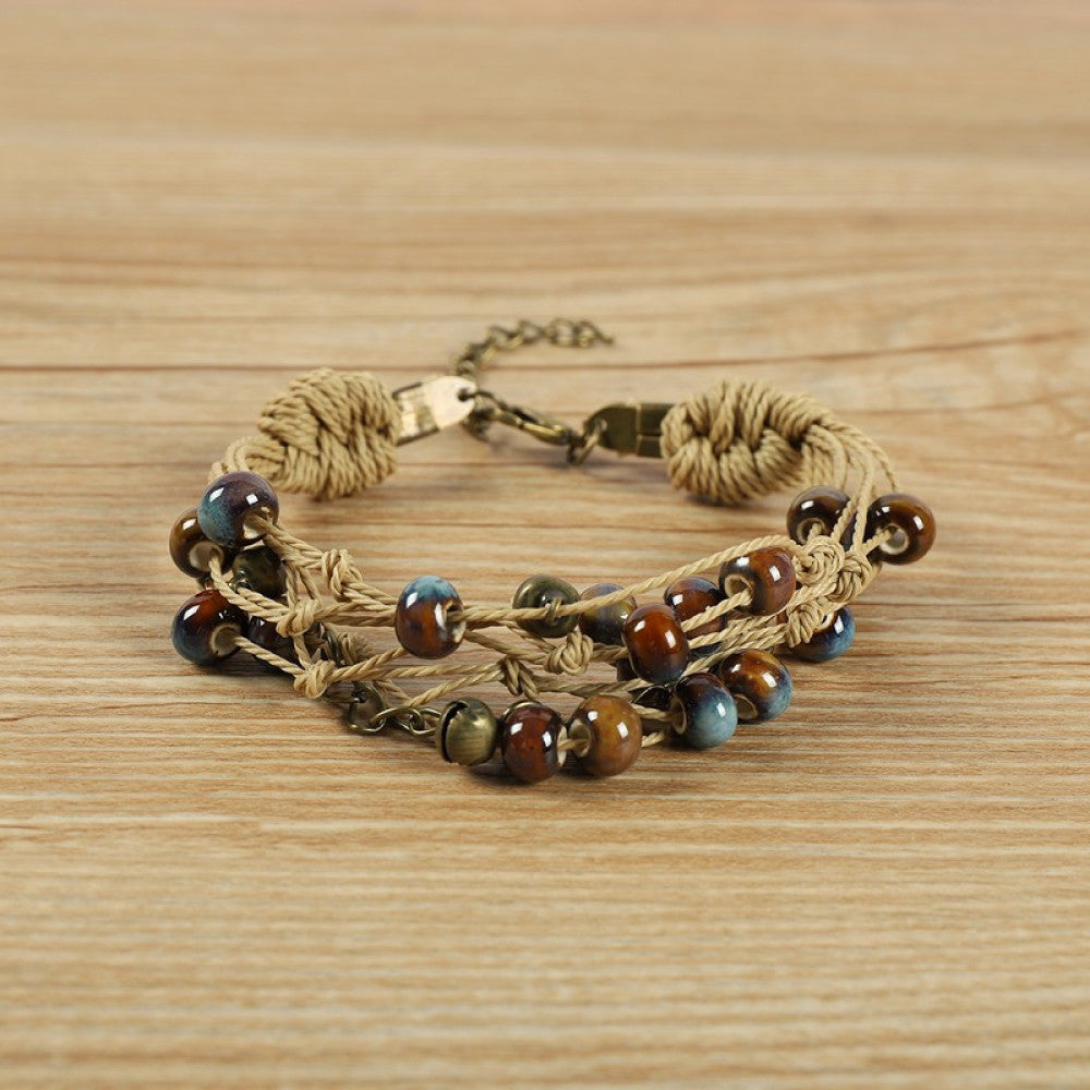 This bohemian multi-layer bracelet features vibrant ceramic beads woven on natural rope, accented with bronze bells and a chain layer. The adjustable clasp ensures a comfortable fit, adding a playful, earthy touch to any outfit