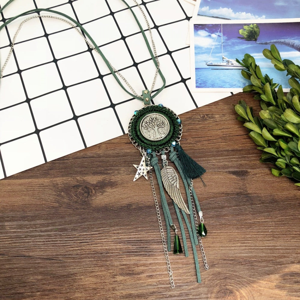 Vintage bohemian blue dreamcatcher necklace with tassel, feather, and geometric accents, displayed on a wooden surface with grid paper and greenery, ideal for boho fashion enthusiasts 02