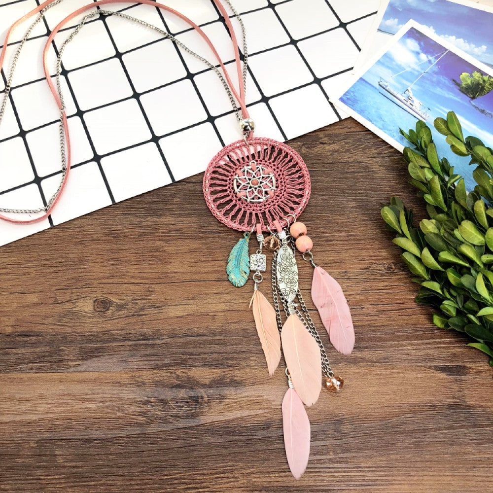 Vintage bohemian blue dreamcatcher necklace with tassel, feather, and geometric accents, displayed on a wooden surface with grid paper and greenery, ideal for boho fashion enthusiasts 04