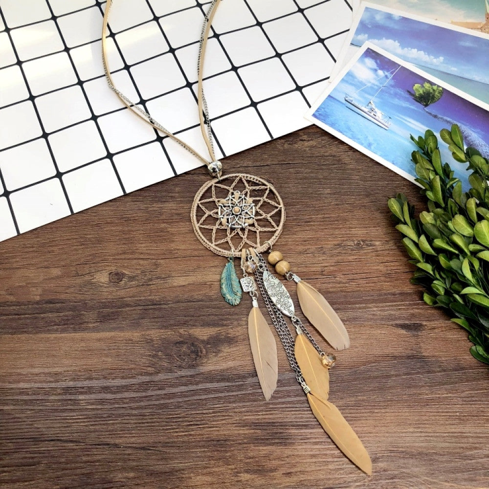 Vintage bohemian blue dreamcatcher necklace with tassel, feather, and geometric accents, displayed on a wooden surface with grid paper and greenery, ideal for boho fashion enthusiasts 05