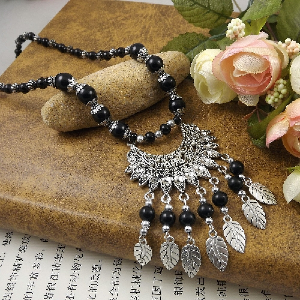 Vibrant colorful beaded necklace with intricate silver-toned leaf tassel and crescent pendant, featuring a mix of bright beads, ideal for bohemian fashion, showcased on a textured surface with floral accents 02