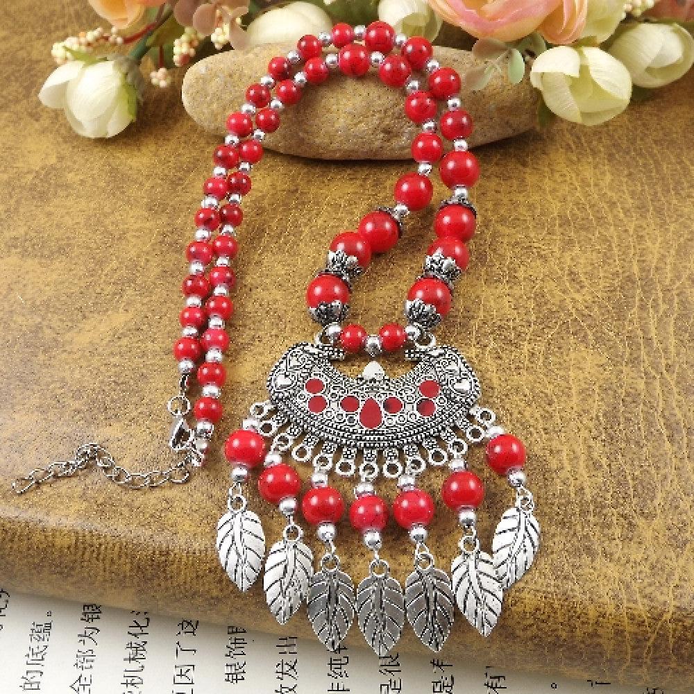 Vibrant colorful beaded necklace with intricate silver-toned leaf tassel pendant, featuring a mix of bright beads and vintage tribal design, ideal for bohemian fashion, showcased on a textured surface with floral accents 04