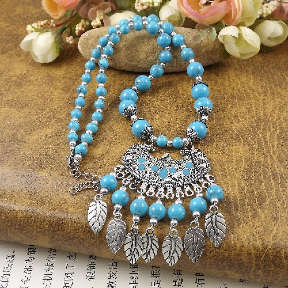 Vibrant colorful beaded necklace with intricate silver-toned leaf tassel pendant, featuring a mix of bright beads and vintage tribal design, ideal for bohemian fashion, showcased on a textured surface with floral accents 05