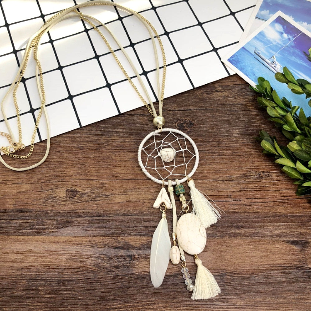Vintage bohemian dreamcatcher necklace with feather, stone, and tassel accents, displayed on a wooden surface with grid paper and greenery, ideal for spiritual boho fashion enthusiasts