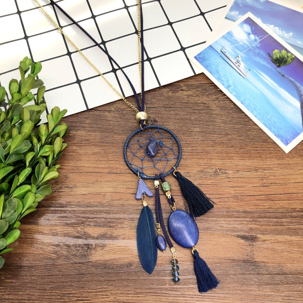 Vintage bohemian dreamcatcher necklace with feather, stone, and tassel accents, displayed on a wooden surface with grid paper and greenery, ideal for spiritual boho fashion enthusiasts 02