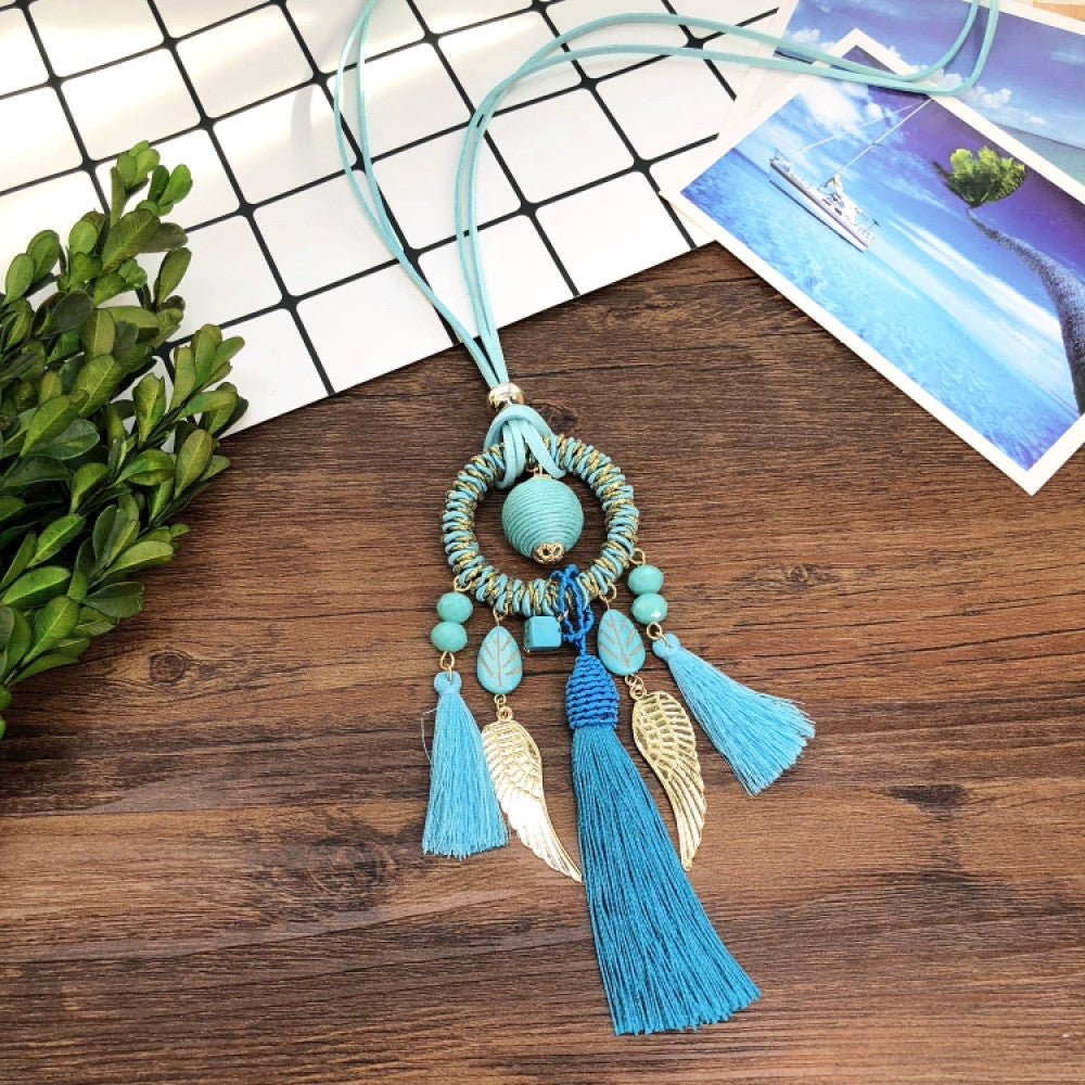 Vintage bohemian dreamcatcher necklace with feather, stone, and tassel accents, displayed on a wooden surface with grid paper and greenery, ideal for spiritual boho fashion enthusiasts 09