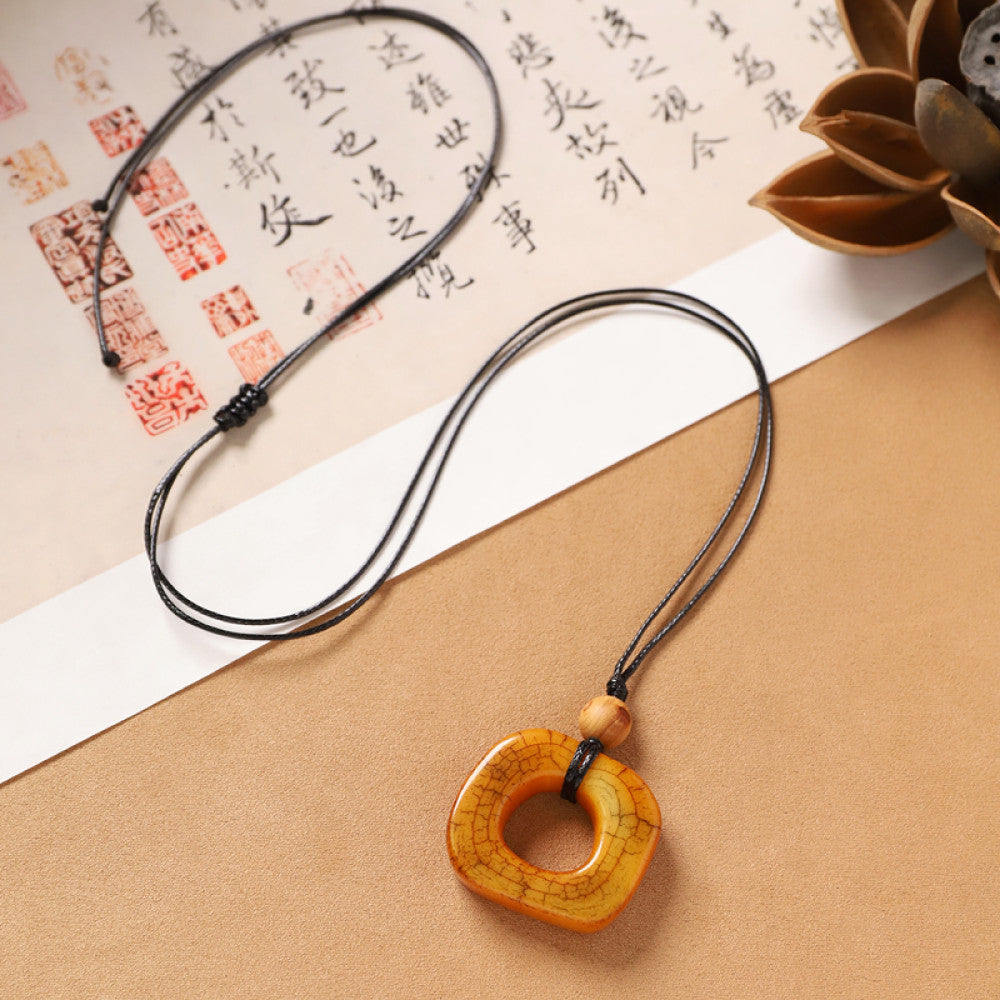 Vintage bohemian ethnic necklace with unique Chinese-style square pendant, featuring earthy tones and black cord, displayed with traditional Chinese calligraphy and decorative flower, ideal for spiritual boho and ethnic fashion enthusiasts
