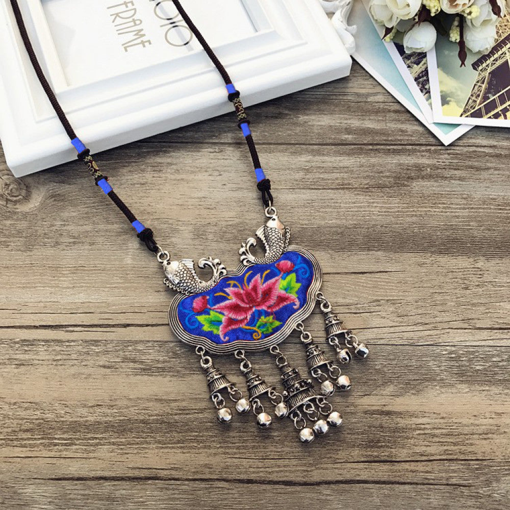 Vintage bohemian ethnic necklace with colorful enamel floral pendant and silver bell tassels, displayed on a wooden surface with decorative accents, ideal for boho fashion enthusiasts 02