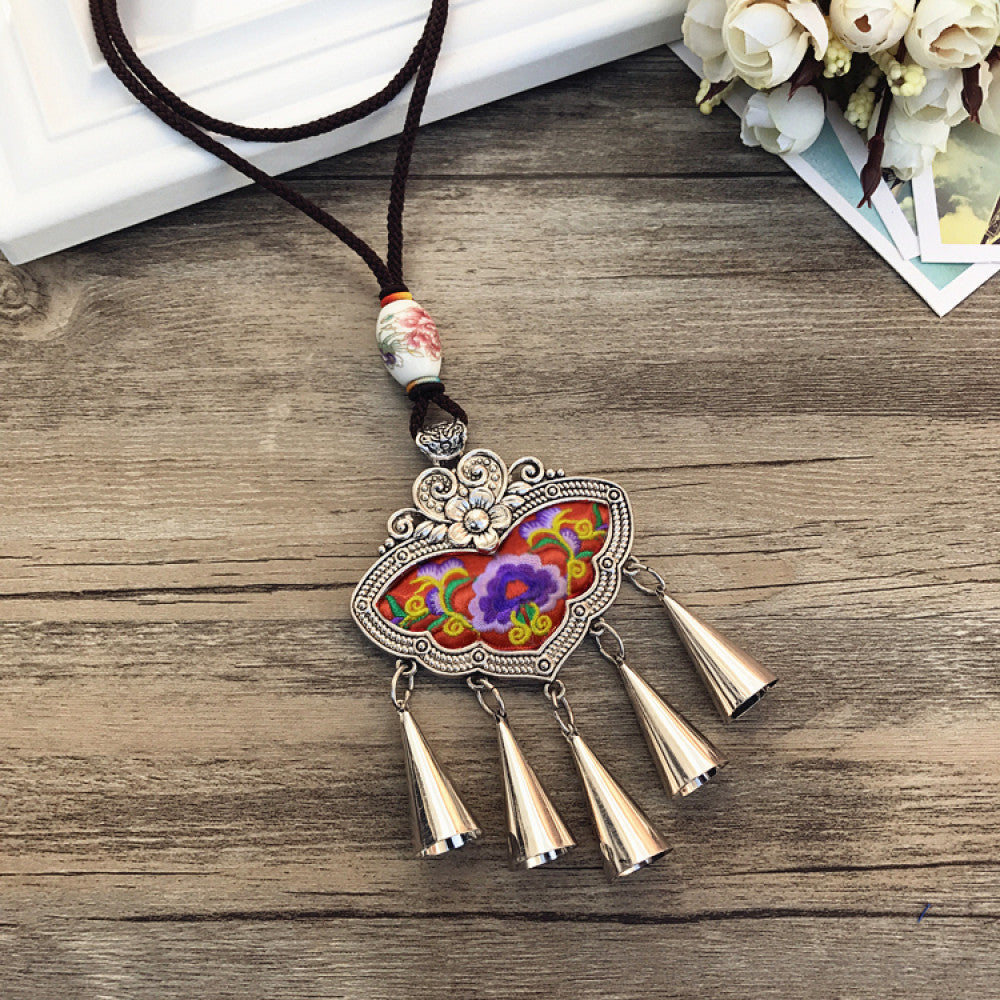 Vintage bohemian ethnic necklace with colorful enamel floral pendant and silver bell tassels, displayed on a wooden surface with decorative accents, ideal for boho fashion enthusiasts 05