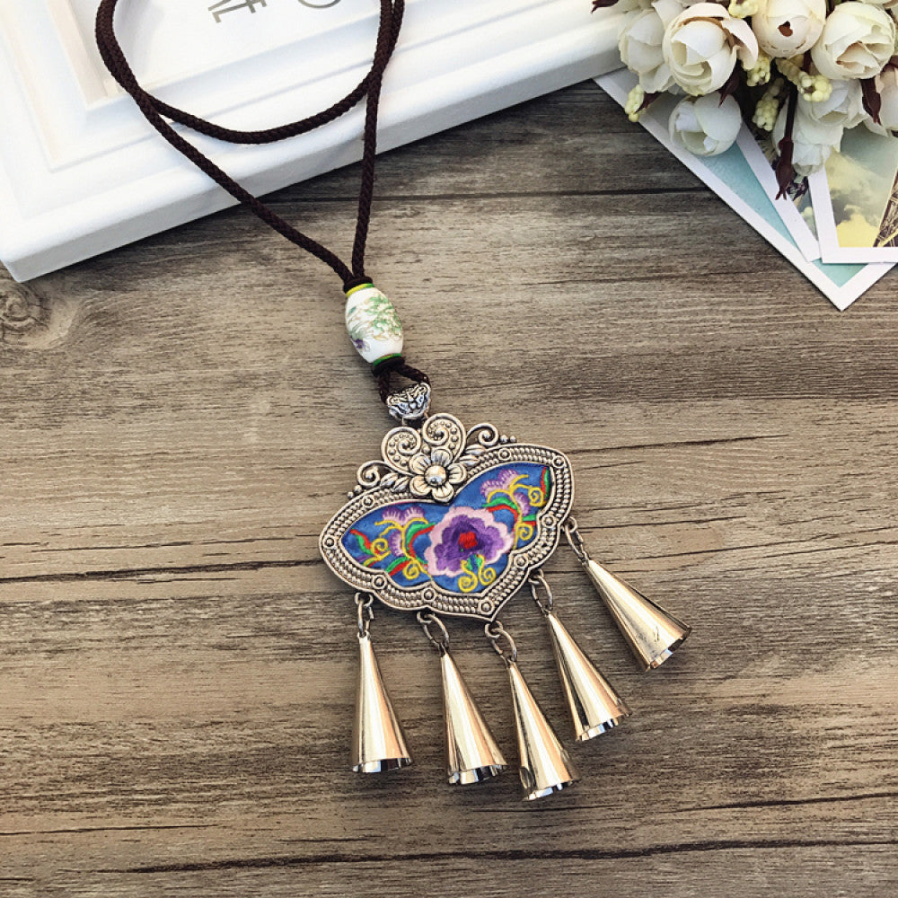 Vintage bohemian ethnic necklace with colorful enamel floral pendant and silver bell tassels, displayed on a wooden surface with decorative accents, ideal for boho fashion enthusiasts 09