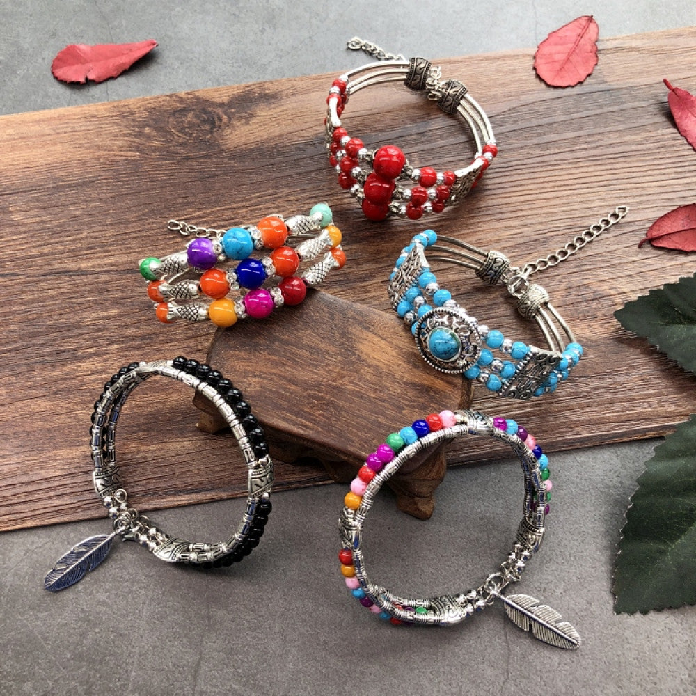 Assorted bohemian vintage ethnic beaded bracelet set with red, multi-color, turquoise, black bead designs and silver accents, displayed on wooden and gray surfaces with leaf decor, ideal for boho fashion enthusiasts