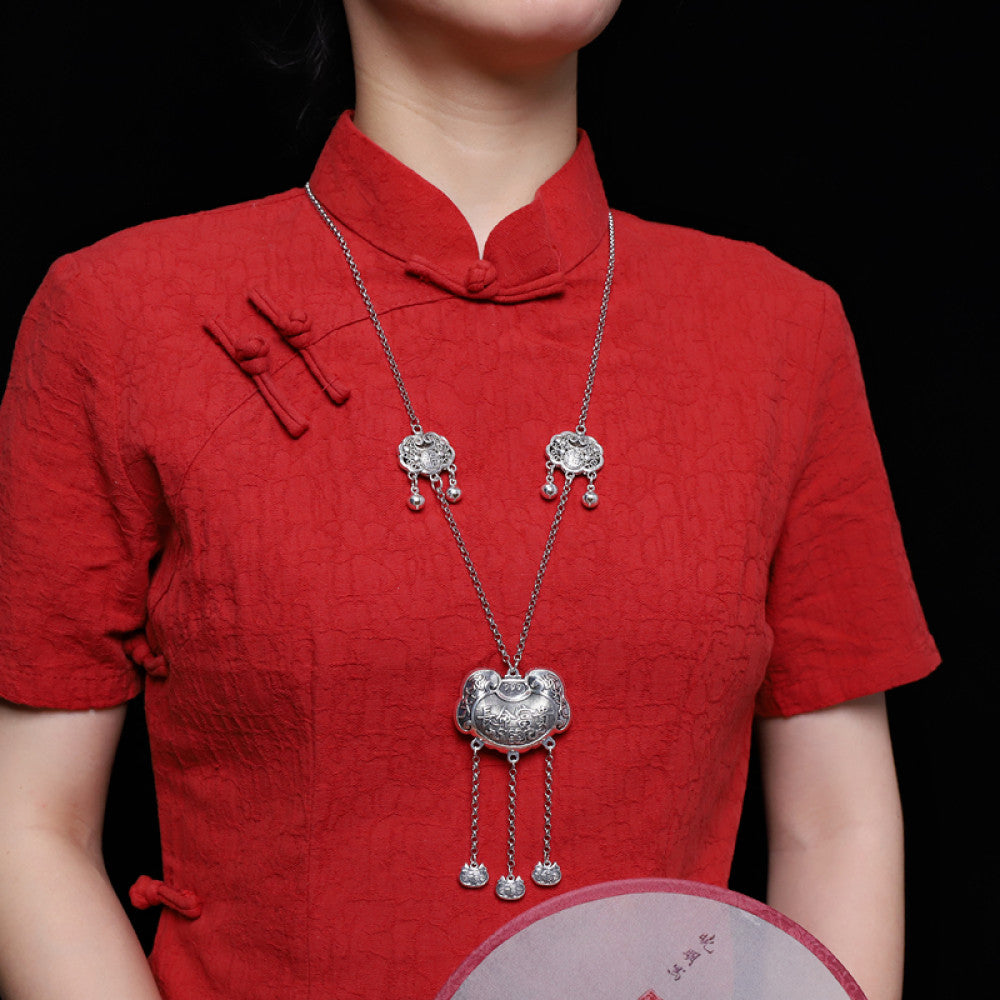 Vintage bohemian ethnic silver lock necklace and earring set with intricate filigree and tassel details, styled with a red Chinese cheongsam, ideal for boho and traditional fashion enthusiasts