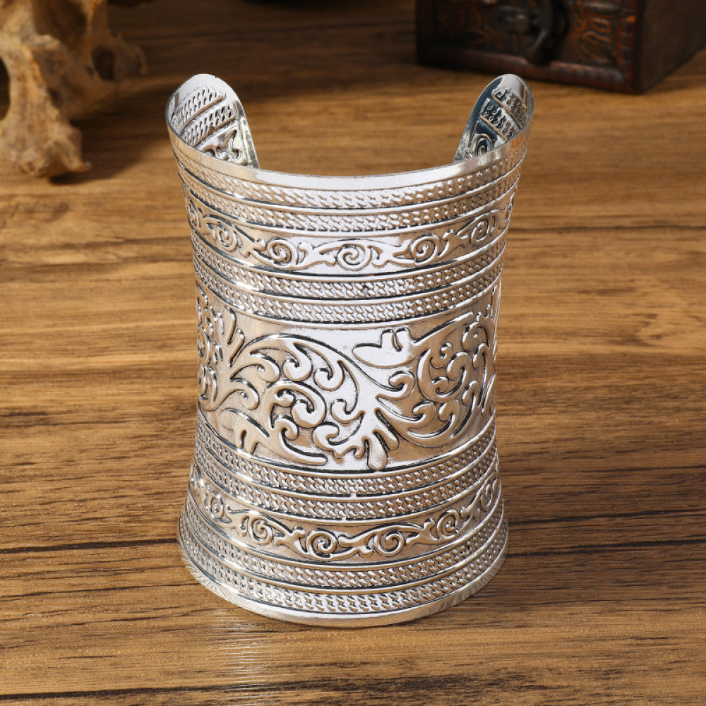 Vintage bohemian ethnic silver-tone engraved cuff bracelet with ornate tribal designs, displayed on a wooden surface with decorative elements, ideal for boho and ethnic fashion enthusiasts