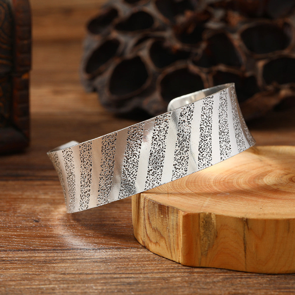 Vintage bohemian ethnic silver-tone cuff bracelet with intricate engraved floral designs, displayed on a wooden surface with rustic decor, ideal for boho and ethnic fashion enthusiasts 01