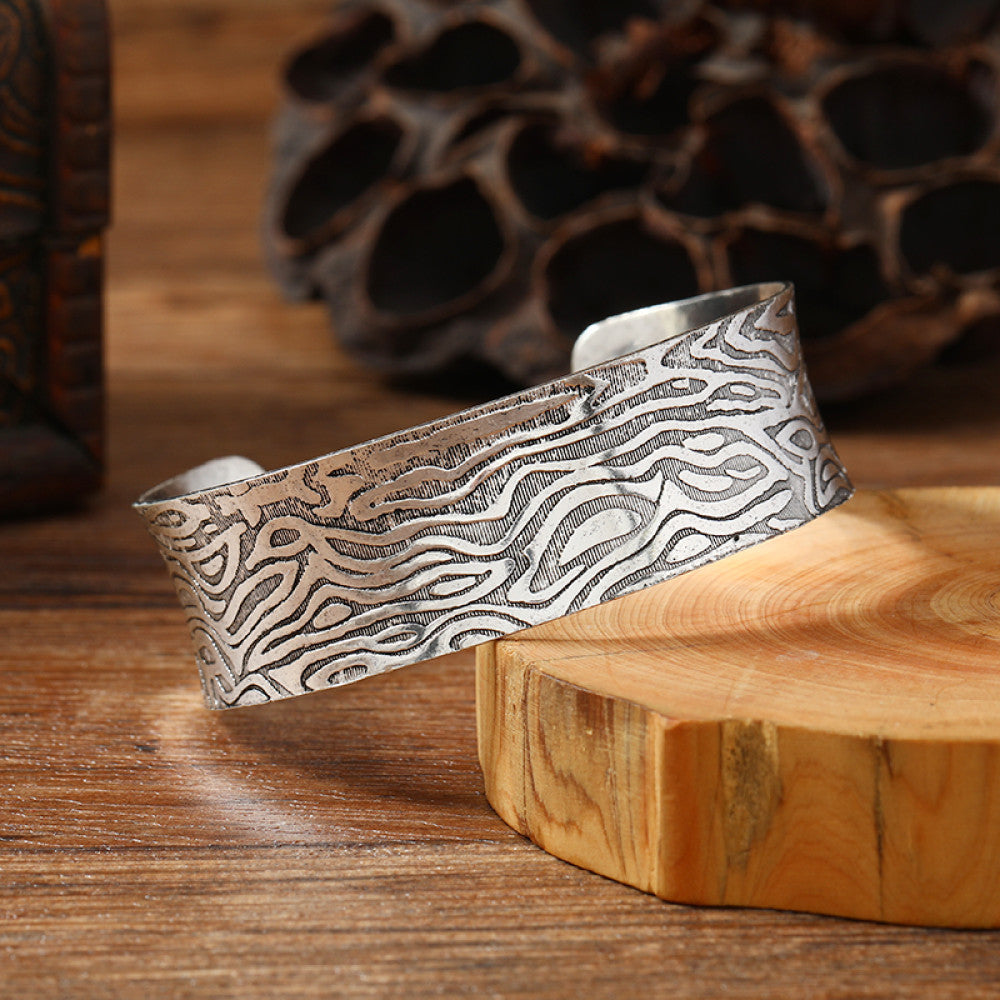 Vintage bohemian ethnic silver-tone cuff bracelet with intricate engraved floral designs, displayed on a wooden surface with rustic decor, ideal for boho and ethnic fashion enthusiasts 08