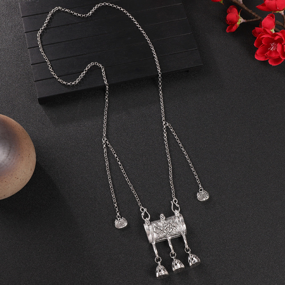 Vintage bohemian ethnic silver-tone necklace with intricate filigree, tassel bells, and ornate pendant, displayed on a dark background with red flowers and decorative accents, ideal for boho and ethnic fashion enthusiasts 04