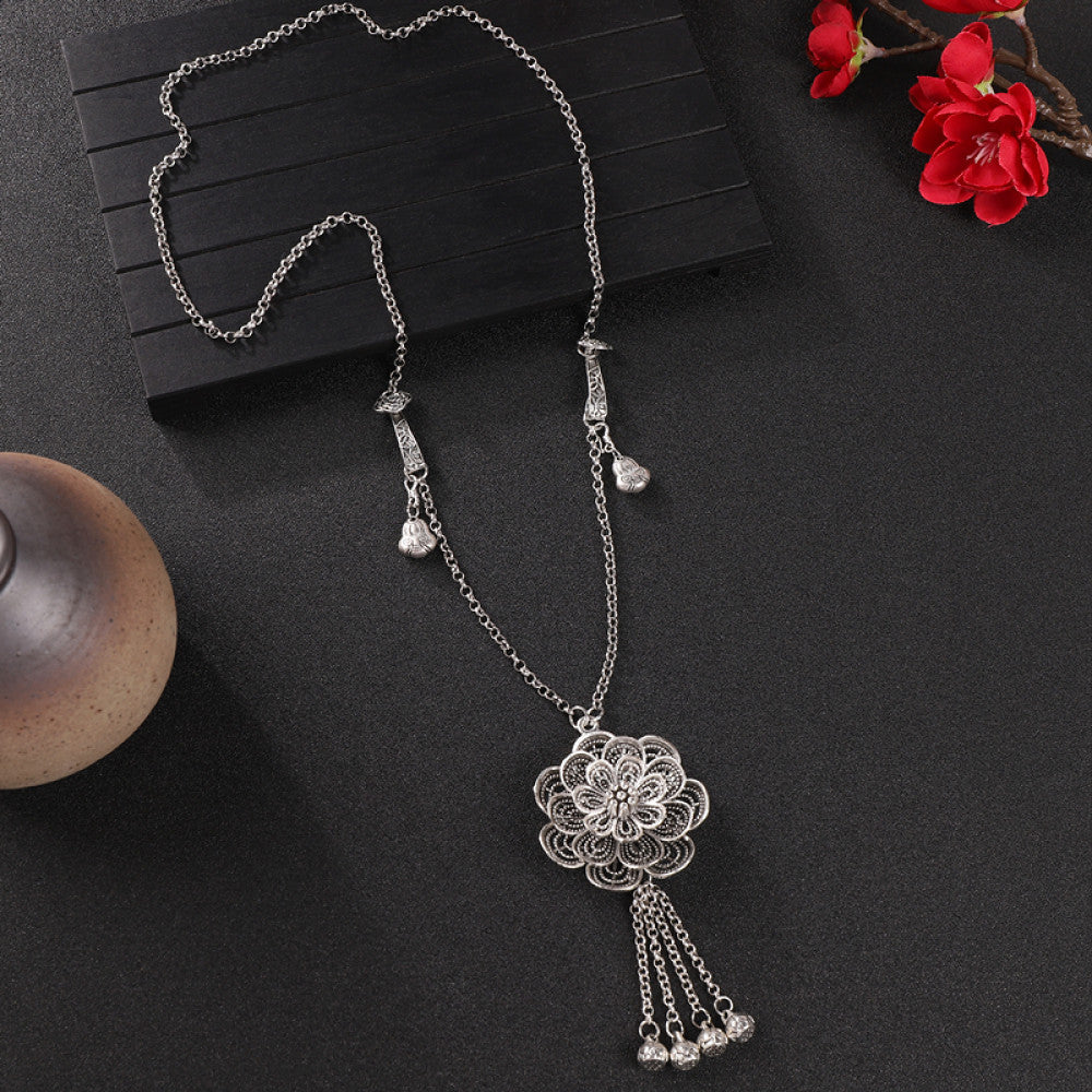 Vintage bohemian ethnic silver-tone necklace with intricate filigree, tassel bells, and ornate pendant, displayed on a dark background with red flowers and decorative accents, ideal for boho and ethnic fashion enthusiasts 05