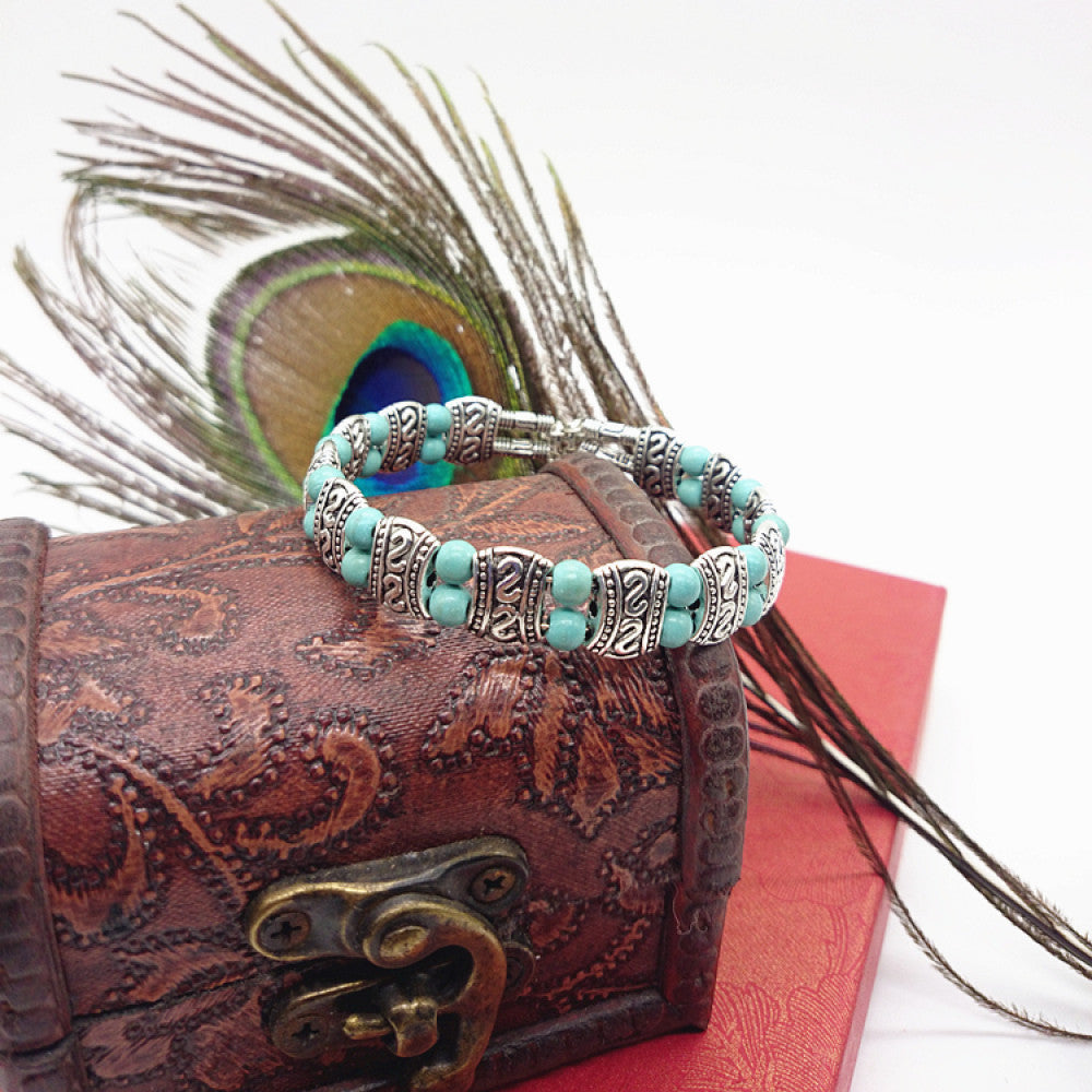 Vintage bohemian ethnic turquoise beaded bracelet with silver engraved accents, displayed on a patterned vintage box with peacock feathers, ideal for boho and ethnic fashion enthusiasts