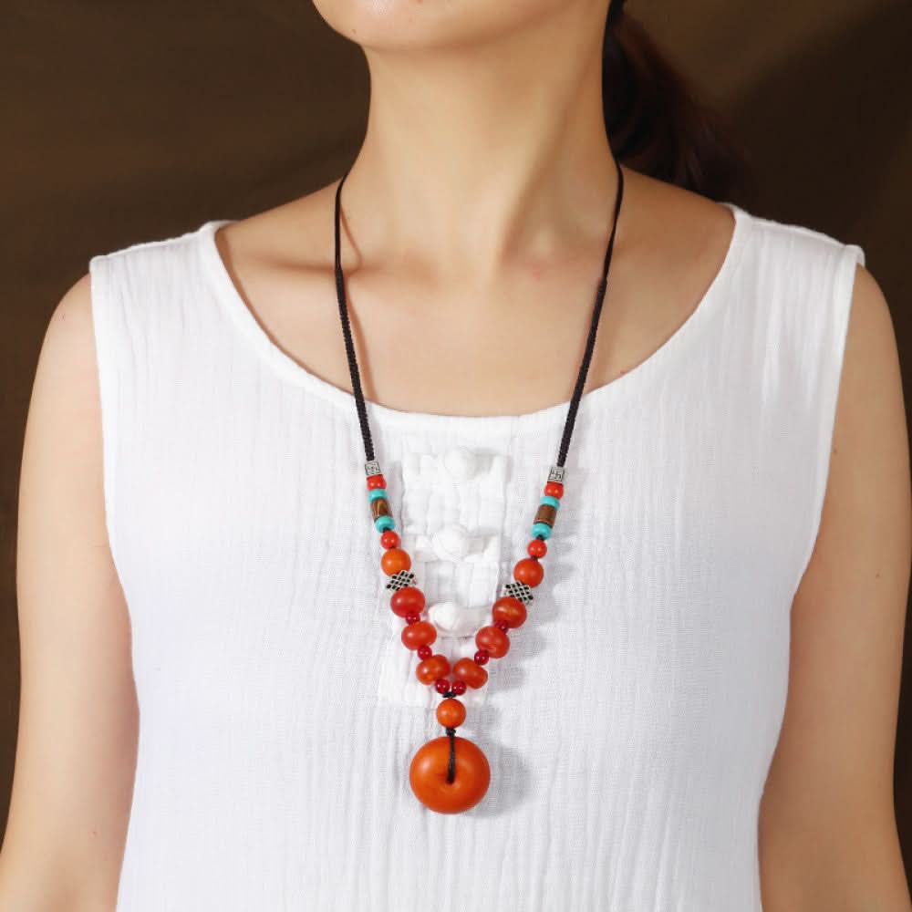 Vintage bohemian ethnic tribal necklace with wooden flower pendants and red beads, featuring a braided rope design, displayed with driftwood and red flowers for a nature-inspired boho look 03