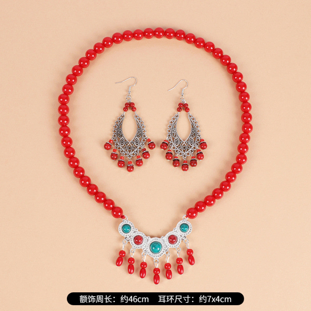 Boho red beaded choker necklace featuring smooth red bead strands, silver-tone decorative centerpiece (with turquoise & red gemstone accents), and red tassel pendants, displayed on a light beige background with red floral decor, ideal for bohemian and traditional fashion enthusiasts in the US 01