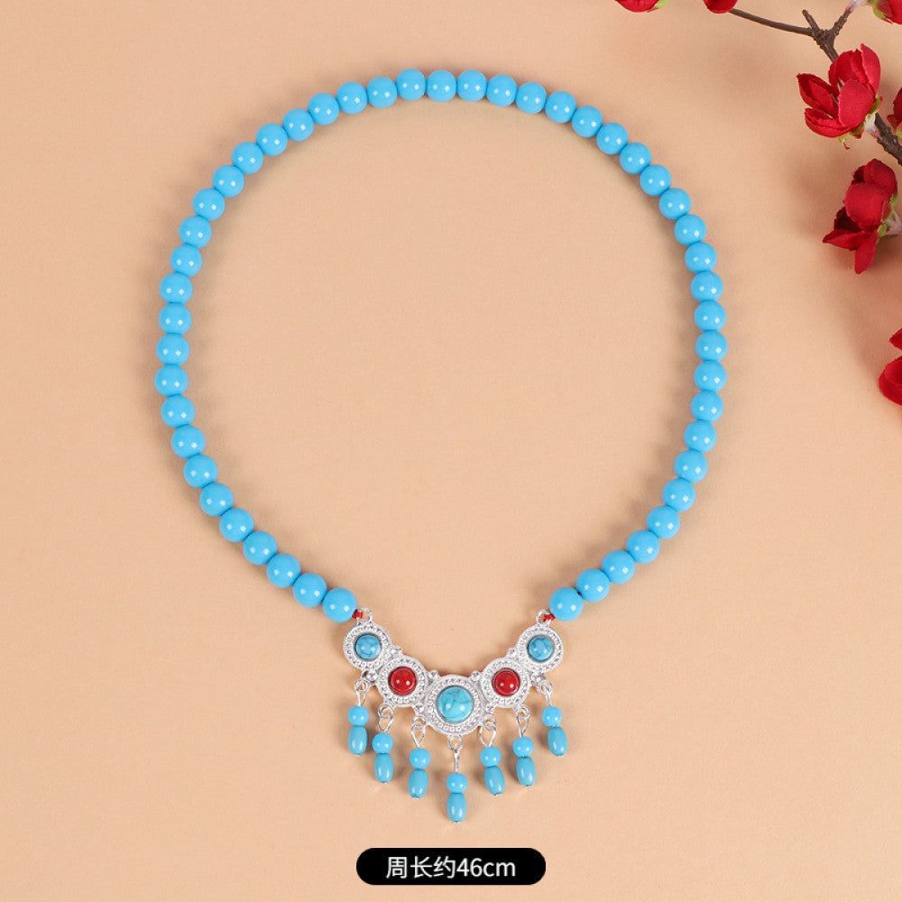 Boho red beaded choker necklace featuring smooth red bead strands, silver-tone decorative centerpiece (with turquoise & red gemstone accents), and red tassel pendants, displayed on a light beige background with red floral decor, ideal for bohemian and traditional fashion enthusiasts in the US 03