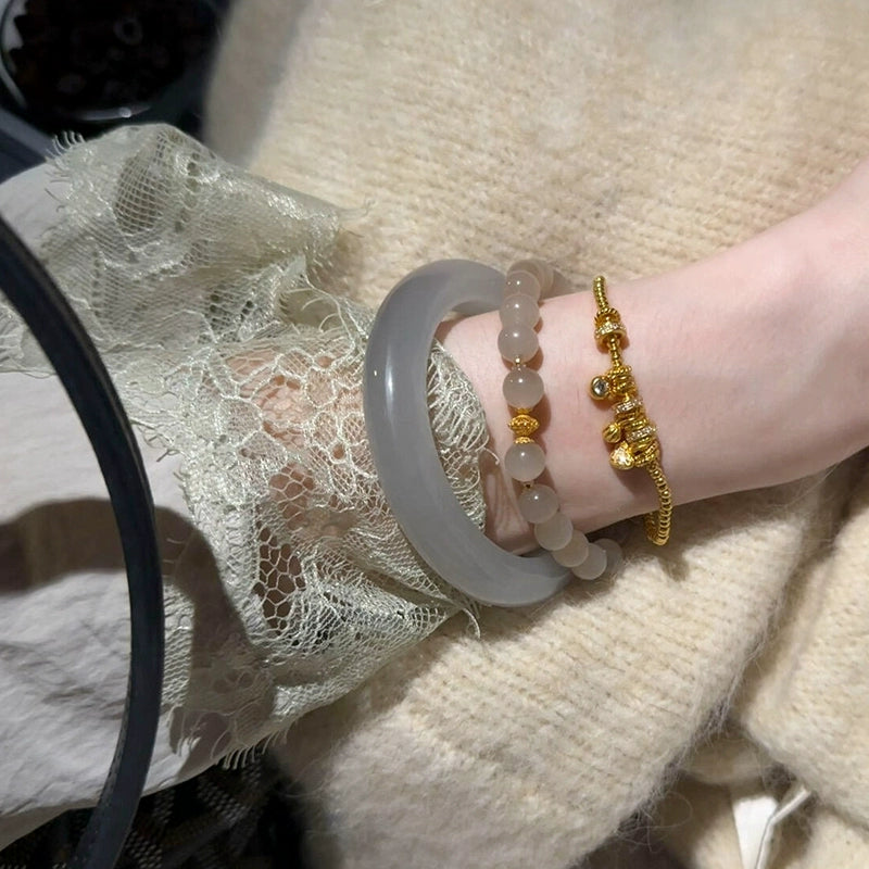 Woman wearing boho stackable bracelets set - grey jade bangle, beaded bracelet, and gold charm bracelet on wrist