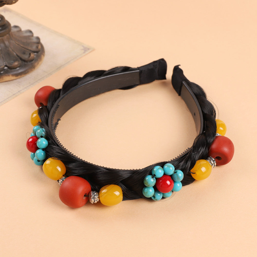 Boho vintage ethnic black braided hair hoop headband (displayed on a soft beige surface with a decorative ornament aside) featuring a prominent gold ornament, plus red, turquoise, and yellow bead details, ideal for bohemian retro ethnic fashion styling in the US 01