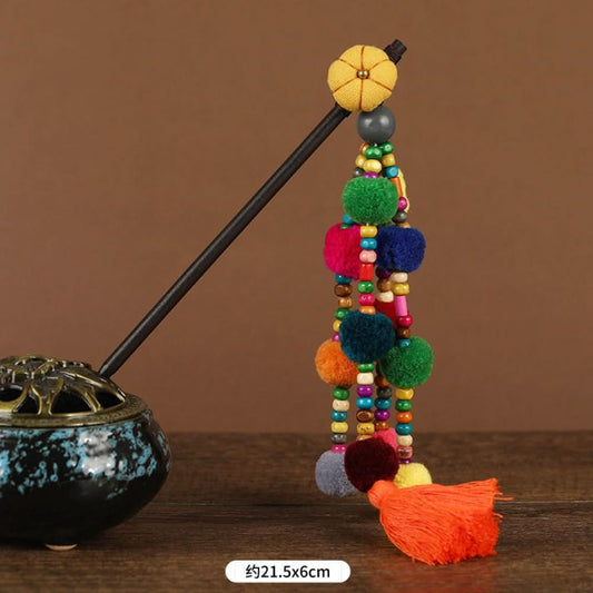 Boho vintage ethnic hair stick pendant featuring colorful pom poms, multi-color beaded accents, and a long orange tassel, displayed alongside an incense burner on a wooden surface against a brown background, ideal for bohemian and traditional fashion enthusiasts in the US