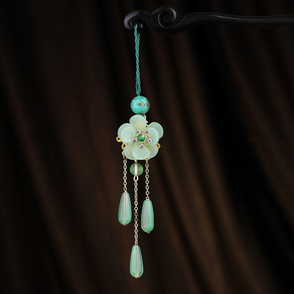Boho vintage ethnic green-tone hair pendant featuring green cord, turquoise bead, white flower-shaped charm (with green gemstone and diamond center, gold trim), and gold-accented green teardrop pendants on chain tassels, styled against a dark brown fabric background, ideal for bohemian and traditional fashion enthusiasts in the US