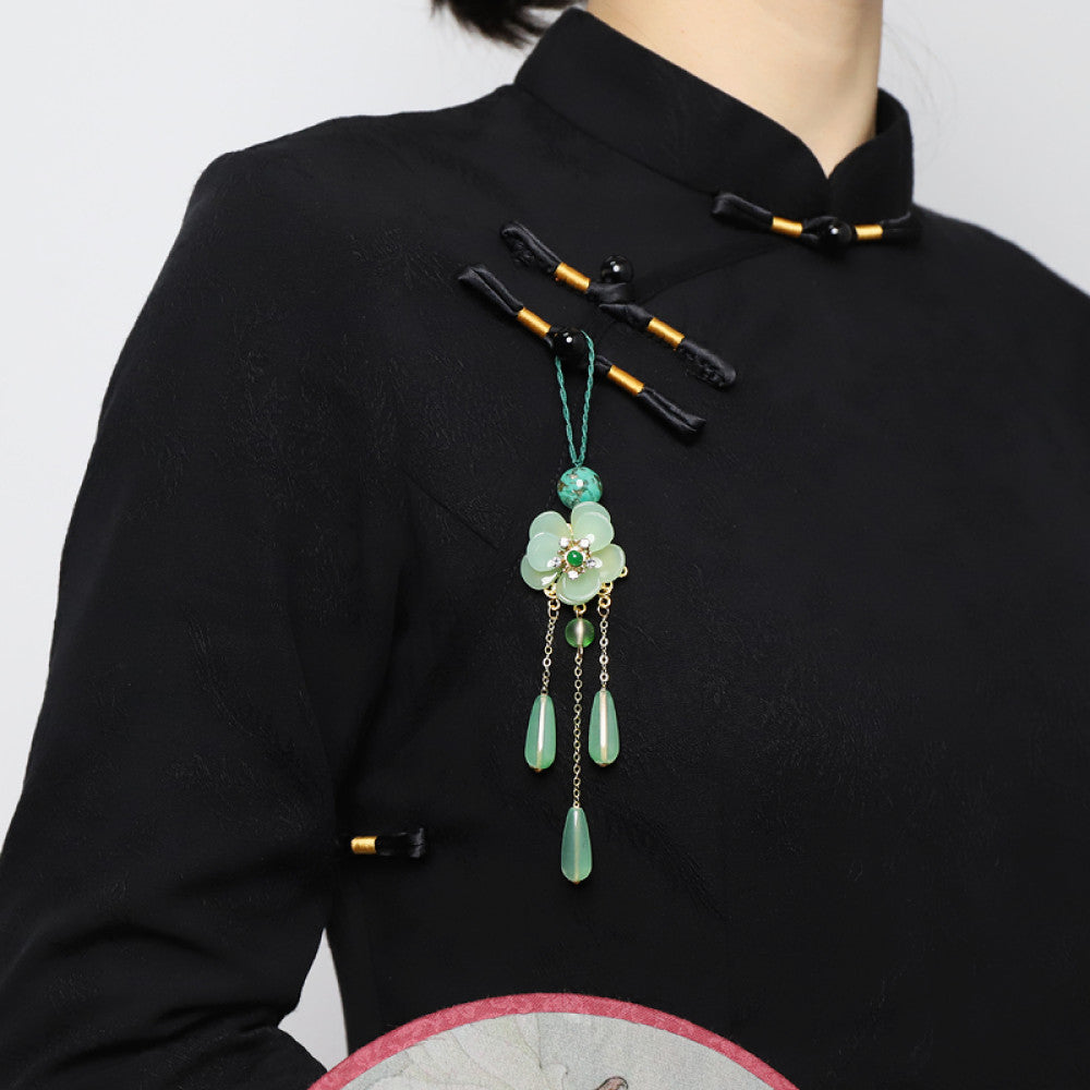 Boho vintage ethnic green-tone hair pendant featuring green cord, turquoise bead, white flower-shaped charm (with green gemstone and diamond center, gold trim), and gold-accented green teardrop pendants on chain tassels, styled against a dark brown fabric background, ideal for bohemian and traditional fashion enthusiasts in the US 01