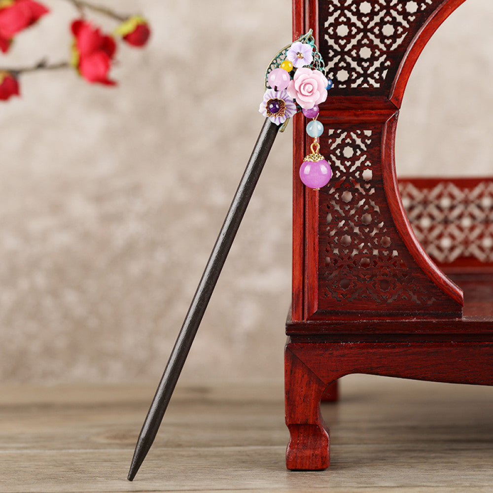 Boho vintage ethnic hair stick featuring a dark wooden-look handle, topped with light green flower, red bead, and green leaf decorative accents, displayed beside a red carved wooden decor (against a background with red florals), ideal for bohemian and traditional fashion enthusiasts in the US 01