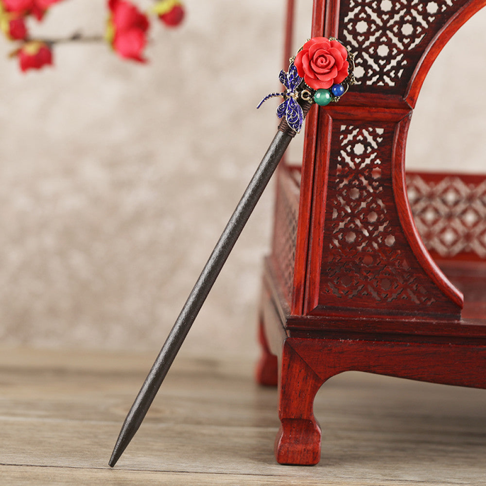 Boho vintage ethnic hair stick featuring a dark wooden-look handle, topped with light green flower, red bead, and green leaf decorative accents, displayed beside a red carved wooden decor , ideal for bohemian and traditional fashion enthusiasts in the US 04