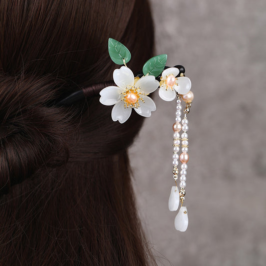 Boho vintage ethnic hair stick ornament (clipped in dark styled hair) featuring a pink flower (red center), green leaf accents, pink/green bead tassel, and light green leaf pendant, displayed against a muted gray background, ideal for bohemian traditional fashion styling in the US 01