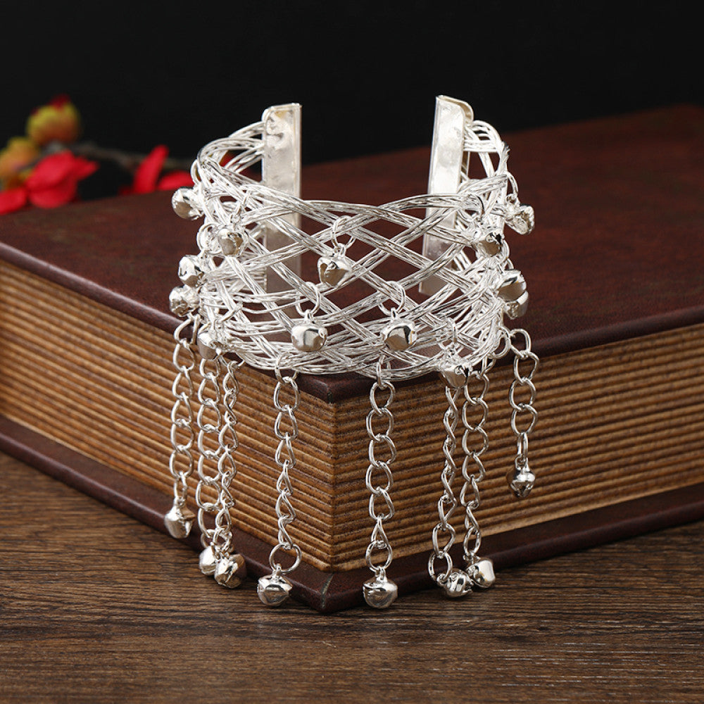 Boho vintage ethnic silver cuff bangle with bell and tassel details, styled on a vintage book, ideal for bohemian and ethnic fashion enthusiasts