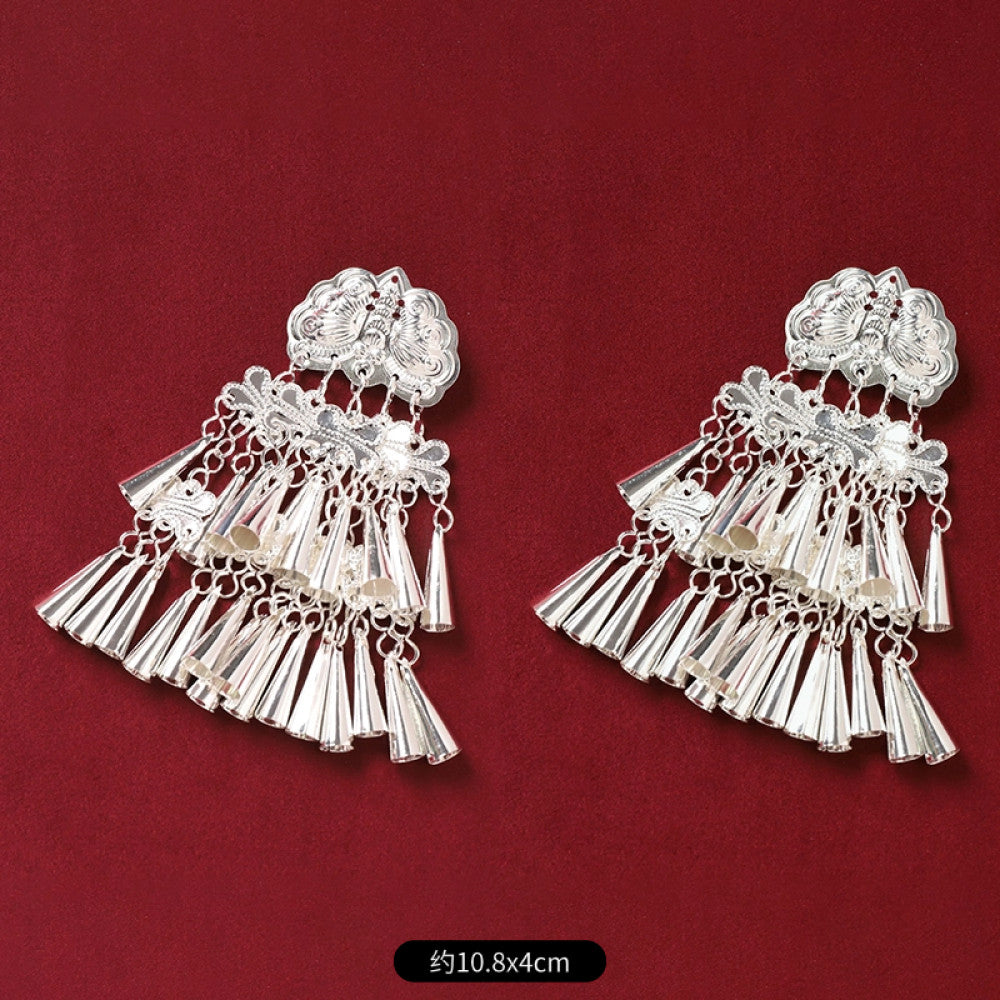 Pair of boho vintage ethnic silver-tone decorative ornaments, featuring intricate butterfly charms and layered bell tassel pendants, displayed on a rich red fabric background