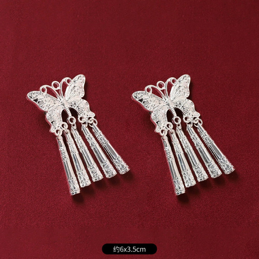 air of boho vintage ethnic silver-tone decorative ornaments, featuring intricate butterfly charms and layered bell tassel pendants, displayed on a rich red fabric background, ideal for bohemian and traditional fashion styling in the US