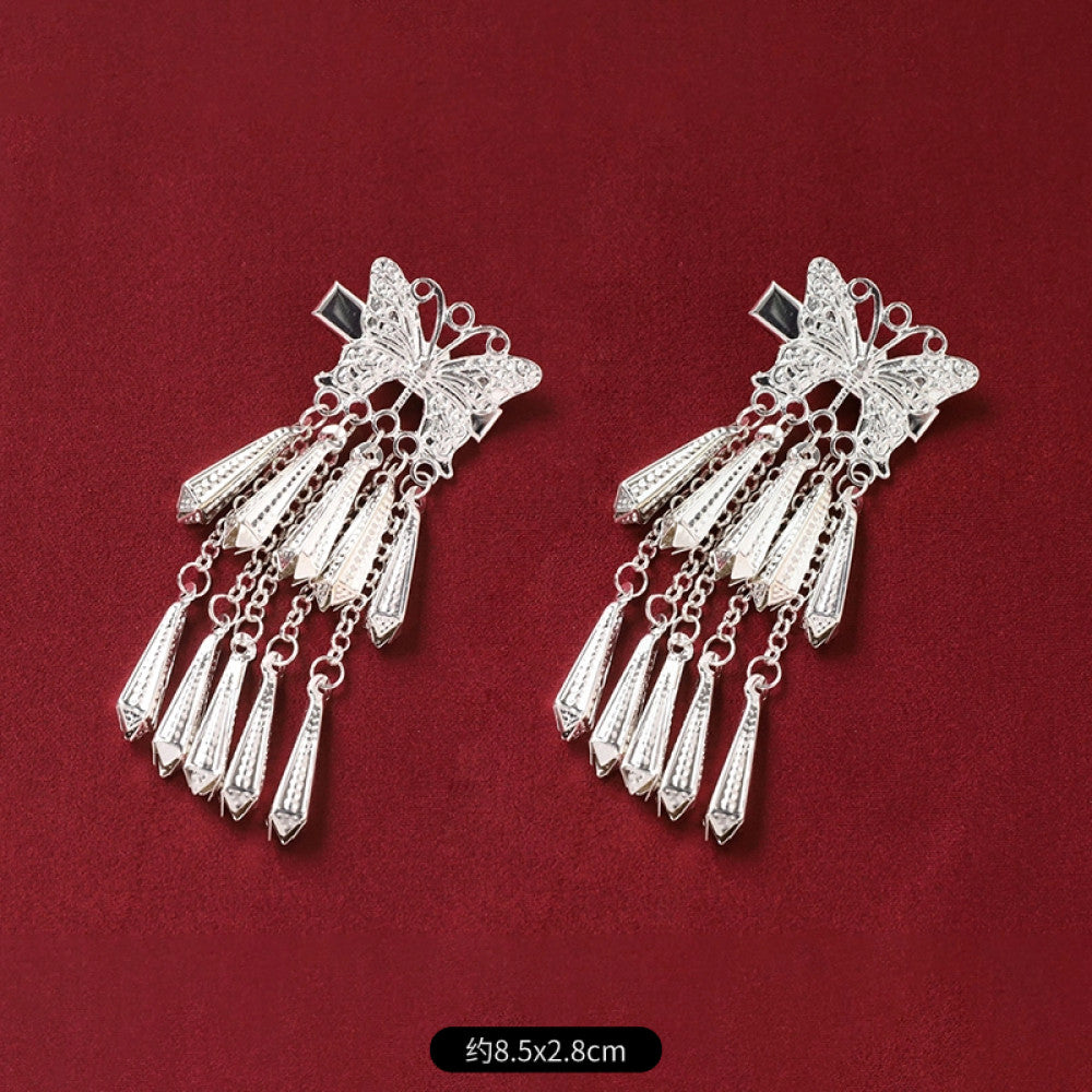 Pair of boho vintage ethnic silver-tone decorative ornaments, featuring intricate butterfly charms and layered bell tassel pendants, displayed on a rich red fabric background, ideal for bohemian and traditional fashion styling in the US 02