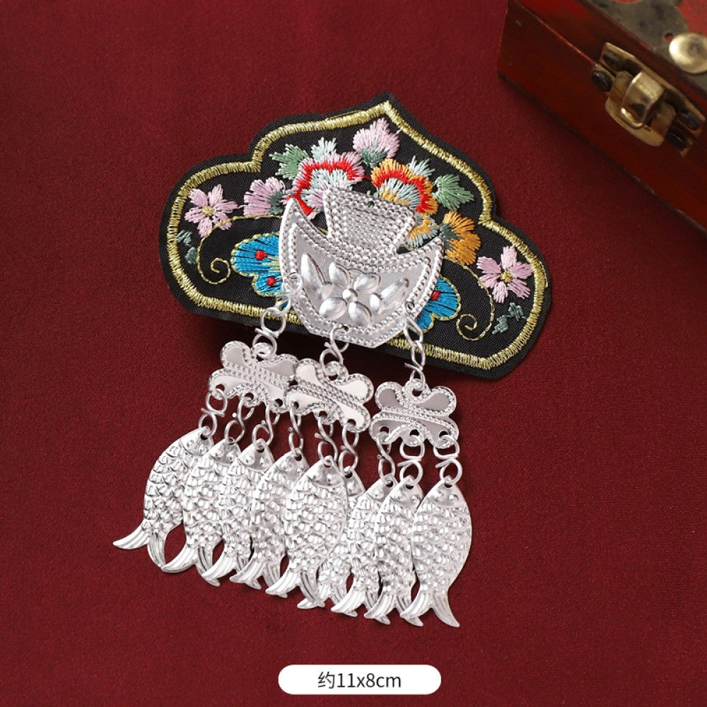 Boho vintage ethnic silver-tone decorative brooch featuring an intricate butterfly charm, pink floral embroidered accent (with blue details), and bell tassel pendants, displayed on a red fabric background 02