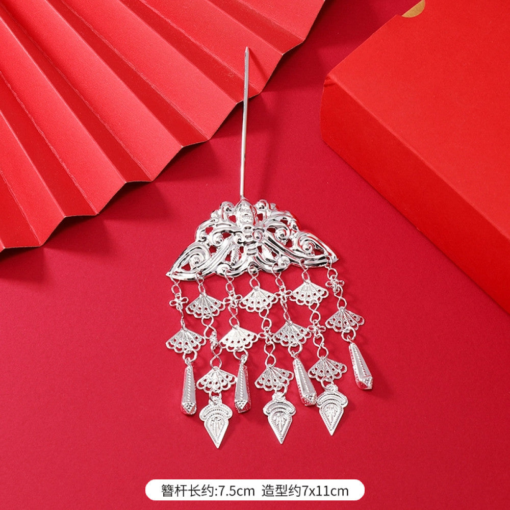 Boho vintage ethnic silver-tone hair stick (hand-held display against a rich red background alongside a red folding fan) featuring intricate openwork details and layered tassel fringe, ideal for bohemian retro or traditional Hanfu fashion styling in the US 01