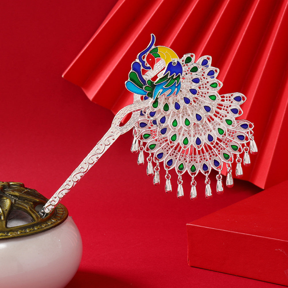 Boho vintage ethnic silver-tone hair stick (displayed with a white vessel & red decorative backdrop) featuring an elaborate peacock openwork design and layered bell tassel fringe, ideal for bohemian traditional fashion styling in the US 01